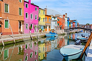 Picturesque colorful idyllic scene with a boats docked on the water canals in Burano Venice Italy. Water reflection