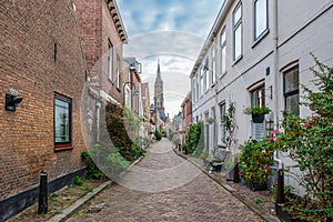 Picturesque Delft cityscape with a view through a narrow ancient alley on the tower of the famous Nieuwe Kerk