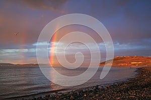 A picturesque evening landscape with a rainbow over a wide river.