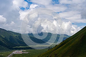 Picturesque, grassy valley surrounded by majestic, towering mountains with fluffy clouds above