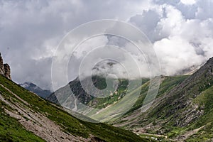 Picturesque, grassy valley surrounded by majestic, towering mountains with fluffy clouds above