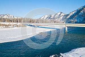 Picturesque landscape in the Altai mountains with snow-capped peaks under a blue sky with clouds in winter with green river and