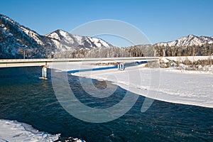 Picturesque landscape in the Altai mountains with snow-capped peaks under a blue sky with clouds in winter with green river and