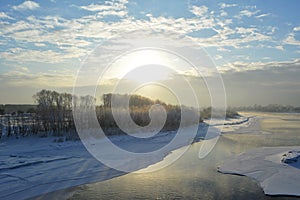 Picturesque landscape with snowy forest on the bank of river with ice in winter