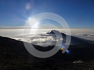 Picturesque landscape view of the top of the mountain in the clouds and bright sun in the blue sky