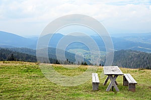 Picturesque landscape with wooden picnic table and mountain forest