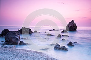 A picturesque magical mystical beautiful scenery with waves and stones in the middle of the sea on the coast at sunset.