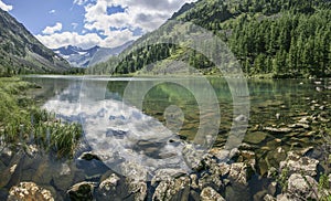 Picturesque mountain lake. Daylight reflected in the water. Forested slopes, stony bottom.