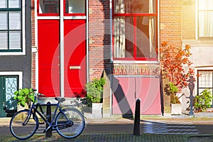 Picturesque in Netherlands. Bicycle near old house with red door and window at the canal with sunlight in Amsterdam, Nord Holland,