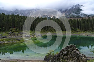 Picturesque peaks of Dolomites mountains in reflection of crystal clear pond surrounded by coniferous forest. Lake of Caresse in