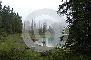 Picturesque peaks of Dolomites mountains in reflection of crystal clear pond surrounded by coniferous forest. Lake of Caresse in