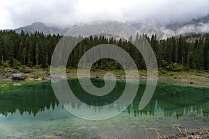 Picturesque peaks of Dolomites mountains in reflection of crystal clear pond surrounded by coniferous forest. Lake of Caresse in