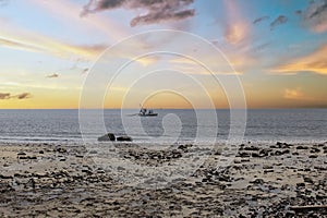 Picturesque scene of a fishing boat passing a beach during a beautiful sunset.