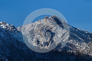 Picturesque snow-capped rocks against the blue sky. The inaccessible mountains are covered in snow during a severe blizzard. Rock