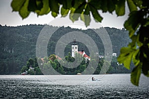 Bled lake with a Church of the Assumption of Mary view, and a girl on a paddleboard, in a frame of leaves in summer day time.