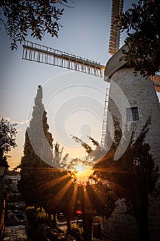 Picturesque sunset glows behind a vintage windmill atop a hill in a rural farm landscape in Jeru