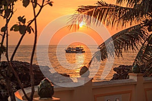 Picturesque sunset near the sea with coconut palm tree, orange sun, boat and clouds. Phu Quoc, Vietnam.