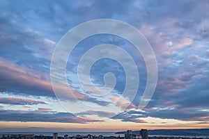 The picturesque sunset sky with blue-orange clouds in the form of stripes over a city. Scenic view of the skyscape at evening