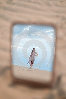 Picturesque view of beautiful blond woman in long casual dress walking in desert