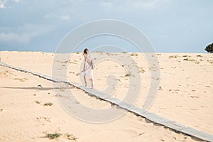 Picturesque view of caucasian blond woman in long long dress walking in desert