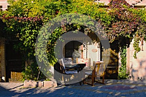 Picturesque view of front yard with outdoor wooden table with four chairs in patio garden with old house.