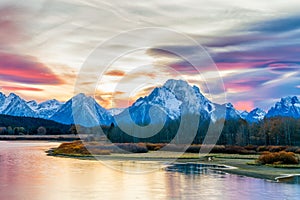 Picturesque view of the grand tetons glowing blue in this autumn sunset. beautiful reflections a smooth in the waters foreground