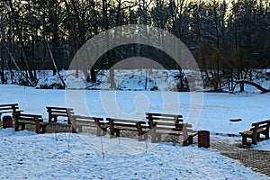 Picturesque view of resting area with wooden empty benches at the lake shore. Scenic winter landscape in the Pushcha-Vodytsia.