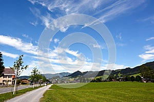 A picturesque view of a small village and a road with houses. In the background are distant mountains of mountains under a blue