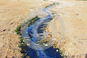 Picturesque view of stream flowing among sandy desert at  background splatters on white background.