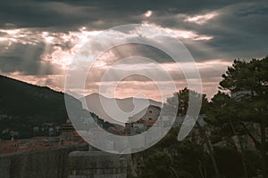 Picturesque view to the ancient mountain town with fortress wall under sunlights shining through the stormy clouds