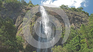 Picturesque waterfall from high rocky cliff with green trees