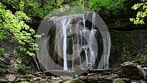 A picturesque waterfall with a small lake in the sunny summer forest