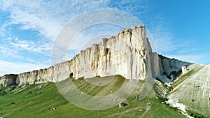 Picturesque white cliff slope, stones and hills near the beautiful green meadow against blue cloudy sky in summer day