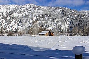Picturesque winter scene featuring a snow-covered field with a rustic barn. Western Montana