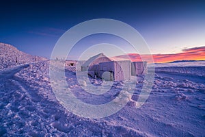 Picturesque winter scene of ice shacks set against a backdrop of snow-covered mountains