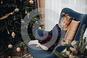 picutre of pretty girl sleeps near the christmas tree on a blue armchair in the living-room