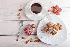 Pie with caramel, white milk sauce and almonds on a white plate on a white wooden background