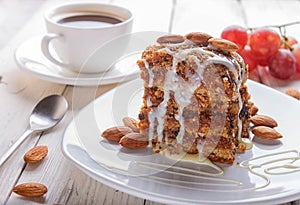 Pie with caramel, white milk sauce and almonds on a white plate on a white wooden background