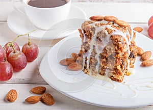 Pie with caramel, white milk sauce and almonds on a white plate on a white wooden background