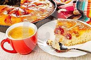 Pie with jam in mold, napkin, cup with espresso, slice of pie, spoon in plate on table