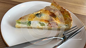 Pie with red fish and broccoli pie featuring red fish and broccoli is served, with a portion placed on a white plate.