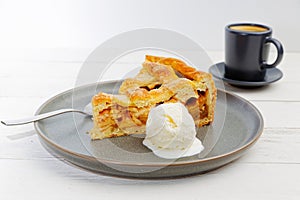 Piece of an apple pie with ice cream and cup of coffee espresso on white wooden table