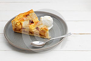 Piece of an apple pie with ice cream on white wooden table.
