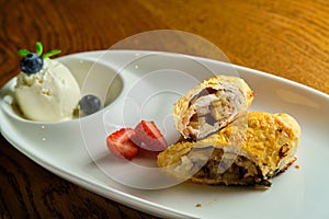 A piece of apple strudel with vanilla ice cream and strawberries