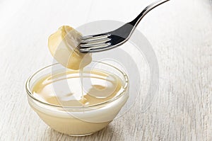 Piece of banana strung on fork above bowl with condensed milk on table