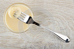 Piece of banana strung on fork on bowl with condensed milk on table. Top view