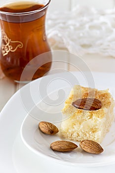 Piece Basbousa Traditional Arabic Semolina Cake with Nuts Orange Blossom Water and glass of tea.