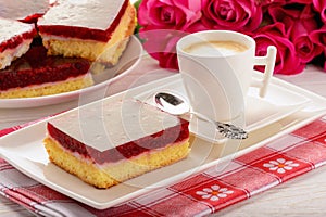 Piece of biscuit cake with cream and cherry jelly and cup of coffee.