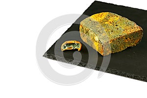 Piece of black bread with green mold and a piece of kiwi with a mold on a black shale board isolated on white background, concept