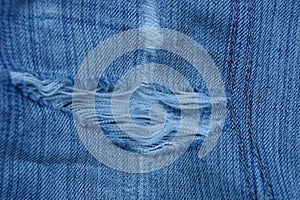 A piece of blue denim pants with white threads on torn fabric